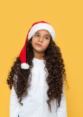 Studio shot of the dark skinned young girl with long curly hair in a Santa Claus hat on a yellow background