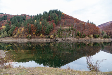 Autumn landscape reflected in the water of the Great Valley ( Valea Mare ) accumulation lake. The lake is located in Gorj, Romania.