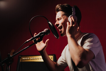 Male singer with headphones and microphone singing song at sound recording studio, music, show business, people and voice concept
