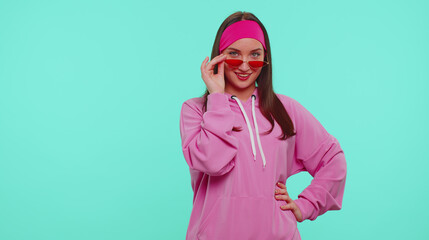 Portrait of seductive cheerful one teen girl in pink hoodie wearing sunglasses, charming smile. People emotions. Young lovely adult woman posing isolated on blue studio wall background