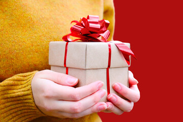 A gift in the hands of a girl. To give gifts. Congratulations. Celebrating Christmas, New Year. A greeting card. A gift box made of craft paper with a red bow.