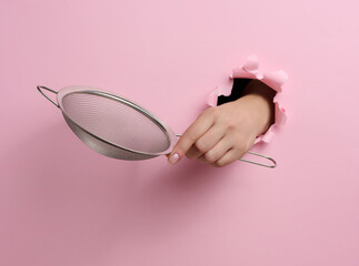 metal sieve for sifting flour in a female hand on a pink background. Part of the body sticking out...