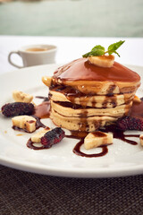 a person taking breakfast  a stack of pancakes with jam and berries and a black coffe