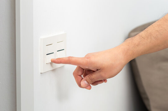 Male right hand is turning on or off on light switch over at the.house or hotel with copy space.