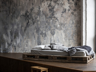 Unfilled bed made of wooden blocks with beige bedding in the bedroom against a wall with Venetian...