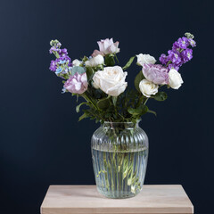 Bouquet of hackelia velutina, purple and white roses, small tea roses, matthiola incana and blue iris in glass vase . Dark blue wall
