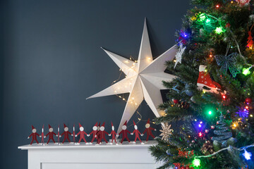 Red paper men holding hands on white and a large paper star on the background of tree there is an artificial fireplace on the background of a dark blue wall as an interior decoration for Christmas