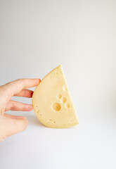 A Piece of Cheese in a Hand on a white background. Studio Shot. Side View. Dairy Food and Cooking at Home Concept for Flyers and Banners