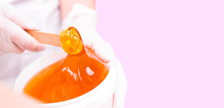 Banner- long format. Close up photo of a bowl with ,shugar paste, shugaring wax gold color hold by a professional specialist woman cosmetologist, skin care concept.