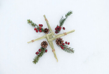 Brigid's cross and fir branches and berries on snow. symbol of Imbolc sabbat. ireland handmade  amulet made from straw. Wiccan tradition for blessed and protected house. flat lay - obrazy, fototapety, plakaty