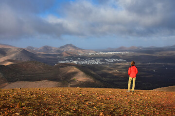 Sunrise in Lanzarote. A woman standing on a mountain, looking to the small towns Yaiza and Uga, surrounded by volcanic landscape. Canary Islands, Spain.