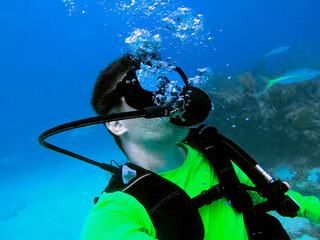 Scuba diver man in lime green t-shirt underwater looking up. Yellowtail snapper fishes around....