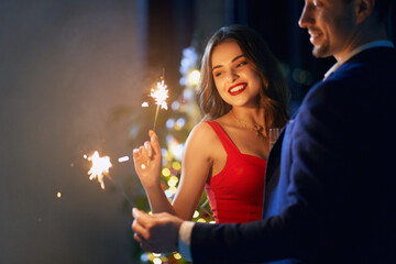Joyful young couple in stylish clothes using sparklers and drinking champagne. Beautiful woman and...
