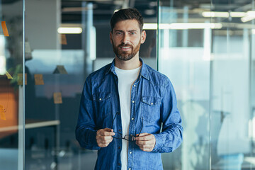 Happy bearded businessman entrepreneur startup owner standing in modern office looking at camera,...
