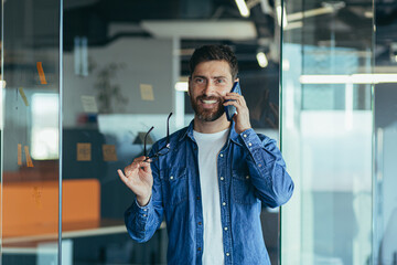 Smiling young adult bearded hipster professional business man making a business call while talking...