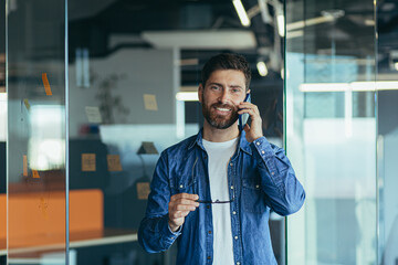 Smiling young adult bearded hipster professional business man making a business call while talking...