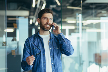 Smiling young adult bearded hipster professional business man making a business call while talking...