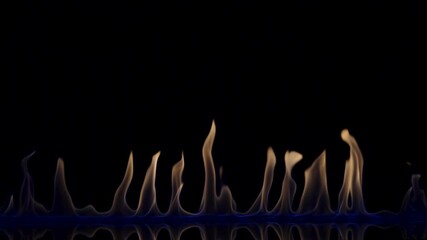 Flammable liquid or petrol stains on black reflective background flash and ignite. An explosion of fire, flaming tongues burning in blue light close up, slow motion. Blaze flames, setting fire to gas.
