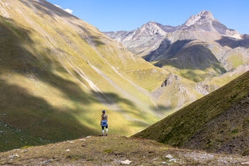Fototapeta premium A woman watching the sharp mountain peaks of the Chaukhi massif form the Chaukhi Pass in the Greater Caucasus Mountain Range in Georgia, Kazbegi Region. The female backpacker enjoys the calmness. Hike
