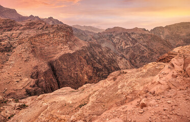 View to rocky landscape with orange pink clouds above, from viewpoint near Ad Deir (The Monastery) in Petra, Jordan