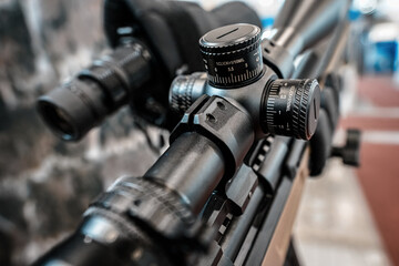 Black shooting scope optics mounted on rifle displayed at weapons exhibition fair, closeup detail...