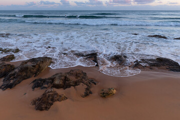 Fototapeta premium Carcavelos Beach after sunset. The last surfers in the ocean. Portugal.