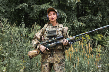 strong woman in camouflage clothing and bulletproof vest stands in field against the background of...