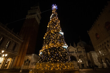 Fototapeta na wymiar Christmas tree with lights and gold colored balls. Colorful background of San Marco square in Venice. Theme concerning the symbols of Christmas