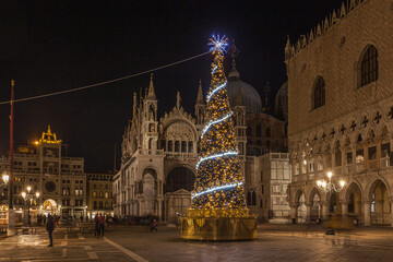 Fototapeta na wymiar Night view of Christmas tree in San Marco square, Venice, Italy. Trail effect of unrecognizable people in motion