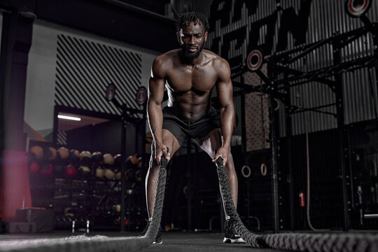afro american fit athlete doing battle ropes exercise at crossfit gym. African Man wear black shorts training with rope. sport motivation, cross fit, fitness concept. cardio training