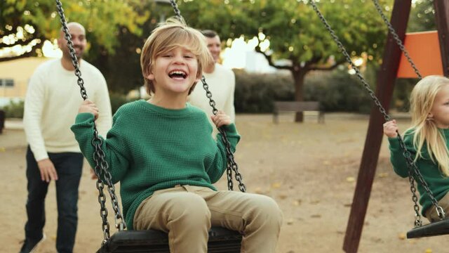 LGBT family - Happy kids and fathers fun swinging on swing at city park