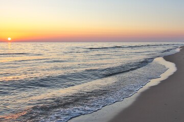Calm seashore in the evening. Hazy sun at sunset.