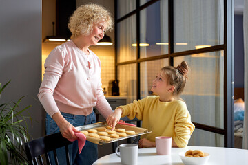 little girl asks to try some cookies by grandmother, after cooking, at home in cozy kitchen...
