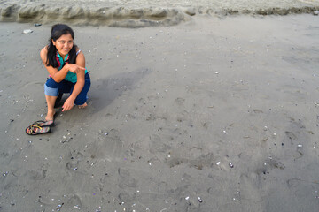 Smiling woman sitting and pointing to the sand on the shore of a beach.