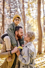 positive couple with son hugging kissing and having fun in autumn park or forest, beautiful and friendly caucasian family spend weekends, holidays together. family, happiness concept