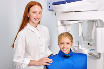Caucasian Redhead Female dental specialist is going to examine an x-ray of child girl in modern dental clinic by professional specialist. little caucasian kid has dentist checkup. Portrait