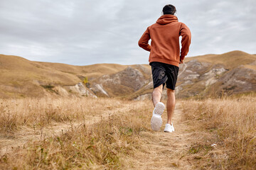 Rear view athletic man sprinter, running on field in sportswear. Sport and fitness motivation. brunette caucasian guy leading healthy lifestyle, keeping fit. in autumn or summer season. in the morning