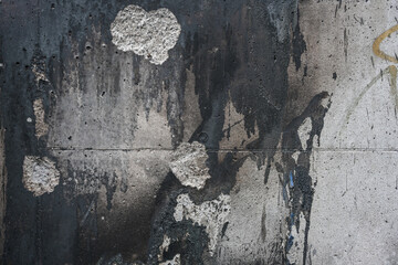 Background texture of a soiled and cracked gray concrete wall with dark paint and fire residue,...