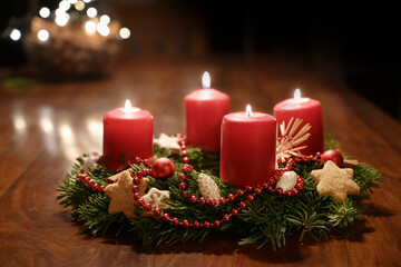 Fourth Advent - decorated Advent wreath from fir branches with red burning candles on a wooden...