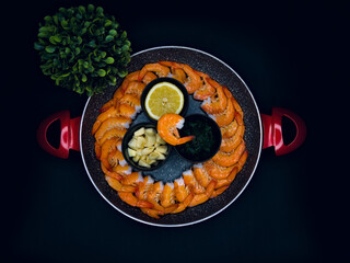 Fresh prawns in a pan with garlic, parsley and lemon on a black background