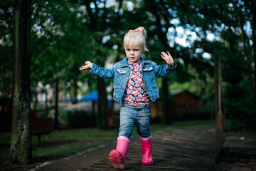 
little cute girl in pink rubber boots on a walk in spring