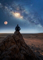 person meditating at night under the Milky Way and Moon back view