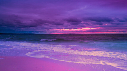Stimmungsvolle stürmische Meereslandschaft bei Sonnenuntergang über der Buzzard Bay auf Cape Cod im Winter. Gesättigte lebendige rosa und grüne Dämmerungslandschaft am Strand. Geschwungene weiße Wellen, die auf den tropischen Strand rollen.