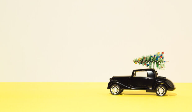 Jagodina, Serbia - November 15, 2021: Classic black car with Christmas tree on the roof on yellow background. Happy New year concept. Copy space.