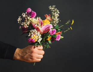 Vintage flower composition made of various autumn flowers and man's hand. Nature concept. Floral Greeting card for Valentines Day or 8 March. Black background.