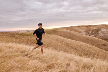 Well-built male running in rural urban field in countryside alone, fitness concept. bearded guy outdoors on fresh air, concentratded on training, active workout. in mountains before sunrise