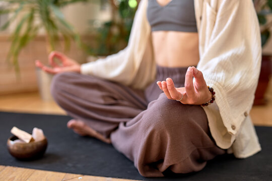 Close-up photo of female hands holding namaste, keeping calm during yoga therapy. Meditation and freedom concept. Zen. Cropped woman sitting on fitness mat meditating