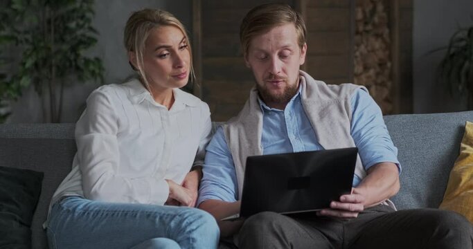Trendy couple business partner working together use laptop at cozy apartment. Man and woman browsing web searching house for rent buying online shopping choosing planning travel weekend leisure