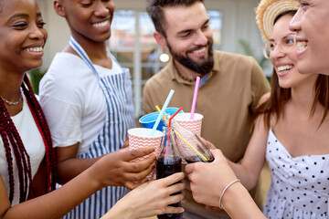 Happy diverse friends having picnic meal with lemonade in nature outdoor. Young people drinking beverages, cheering, dinner in the evening. Youth lifestyle, summer and friendship concept