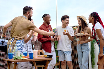 Young positive men and women having barbecue party on the evening on house patio. people doing bbq dinner outdoor cooking meat and drinking lemonade, eating burgers. Food, fun and friendship concept